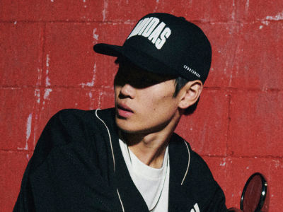 A young man wearing a black cap with the word "VANS" printed on it, standing in front of a red brick wall.