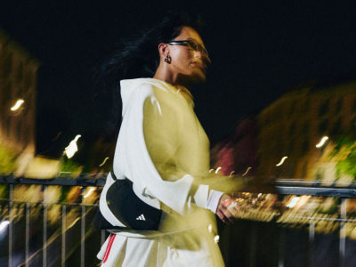 A person in a white jacket stands on a bridge at night, with blurred lights and structures visible in the background.