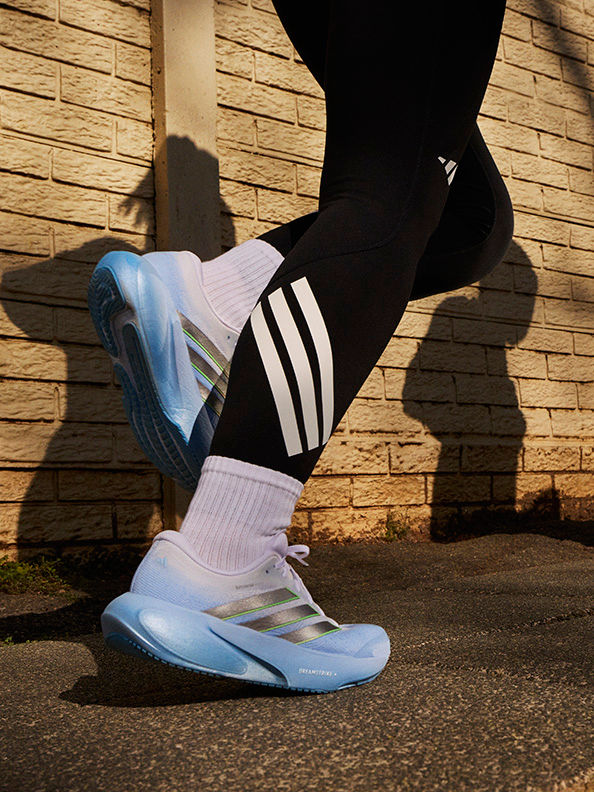 The image shows a person's legs and feet wearing black leggings and blue and white athletic shoes, standing in front of a brick wall.