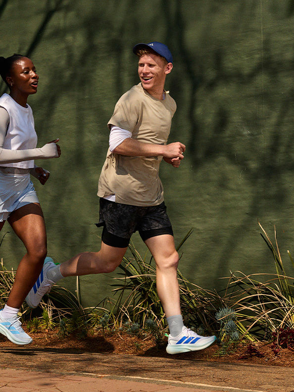 Zwei Menschen laufen auf einem unbefestigten Trail, umgeben von üppiger Vegetation im Hintergrund.