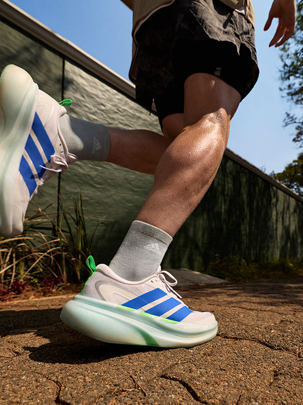 Das Bild zeigt eine Person im unteren Rumpfbereich, die Sportschuhe und -shorts trägt und auf einem unbefestigten Pfad vor einem grasbewachsenen Hintergrund steht.