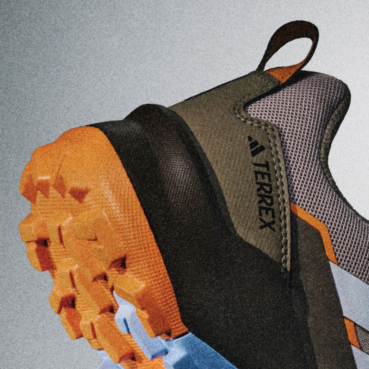 La imagen muestra un primer plano de zapatilla de senderismo o de outdoor con una inconfundible combinación de colores naranja y gris, una suela texturizada y un empeine de malla con el logotipo de "Terrex" visible.