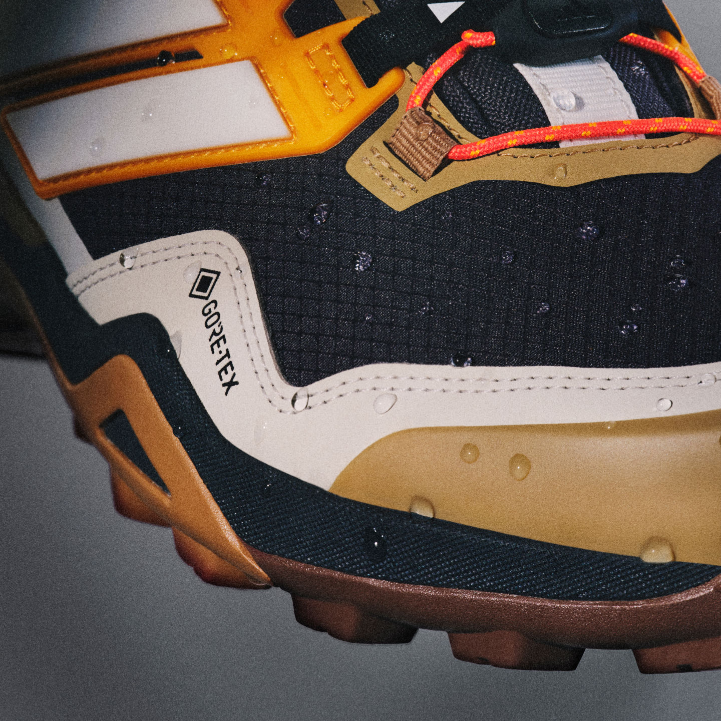 Zbliżenie na mocne, kolorowe buty hikingowe z wyróżniającą się pomarańczową podeszwą i różnymi teksturowanymi materiałami na ciemnym tle.