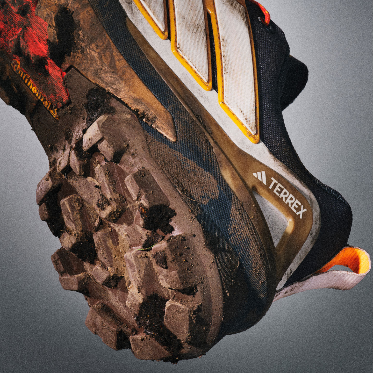 Zbliżenie na mocne, pokryte błotem buty hikingowe z wyróżniającym się logo adidas Terrex na ciemnym, teksturowanym tle.