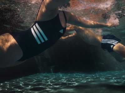 A person in a black swimsuit is submerged in clear, turquoise water, with a rocky, underwater landscape visible in the background.
