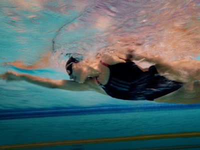 Una persona con un traje de neopreno negro está sumergida bajo el agua, rodeada por un océano vibrante de color turquesa con un fondo borroso.