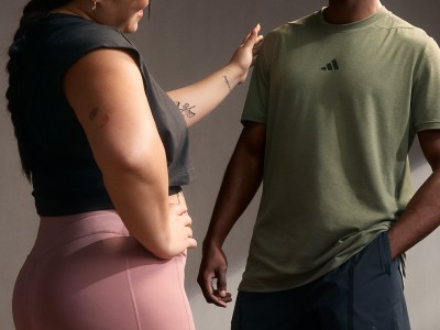 La imagen muestra a dos personas, una persona con una camiseta negra y otra con una camiseta verde, de pie juntas en lo que parece ser un estudio o un decorado interior.
