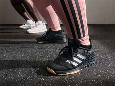 The image shows a person's lower body wearing black and white athletic shoes and pink leggings, standing on a dark, textured surface.