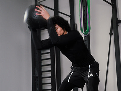 A person in a black outfit is leaning against a metal frame structure in a dimly lit room.