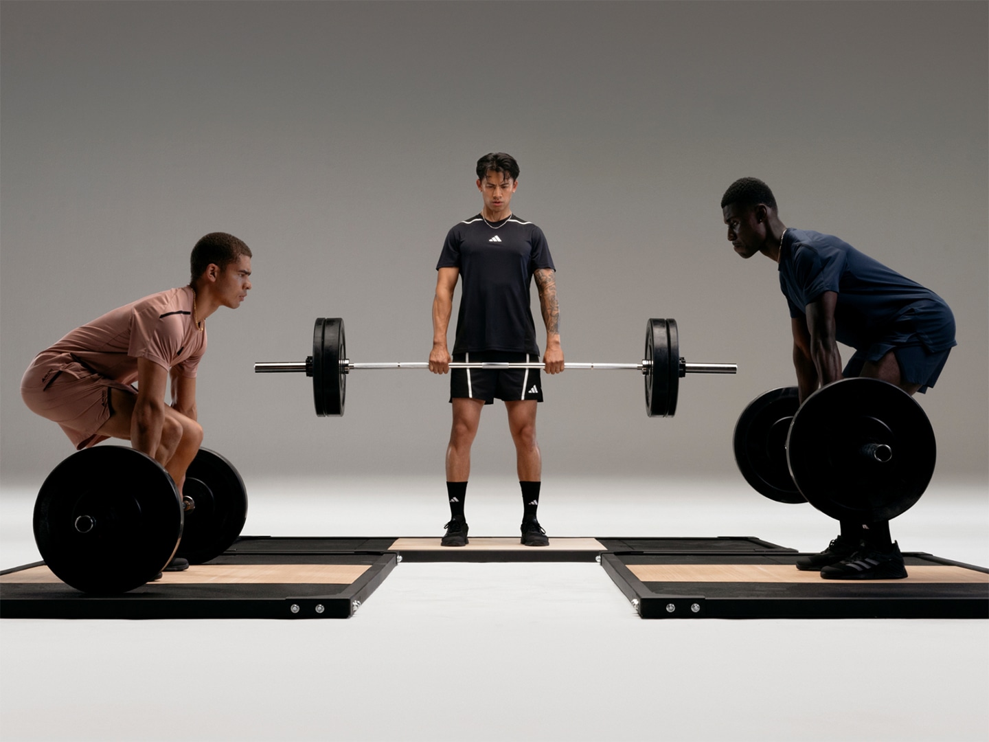Three individuals, two men and one woman, are engaged in weightlifting exercises on a dark, minimalist background.
