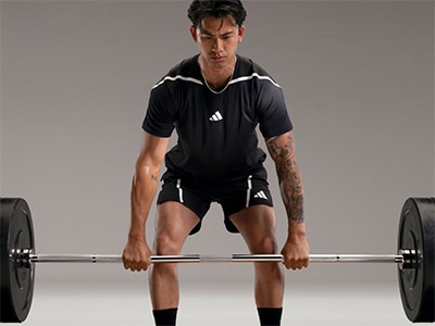 A muscular man in athletic clothing is lifting a heavy barbell in a gym setting.