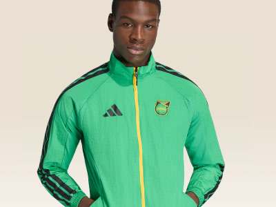 A young man wearing a bright green and yellow athletic jacket with the Adidas logo stands against a plain background.