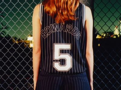 The image shows a person wearing a black and white striped jersey with the number "5" and the name "Edwards" printed on the back, standing in front of a green chain-link fence.