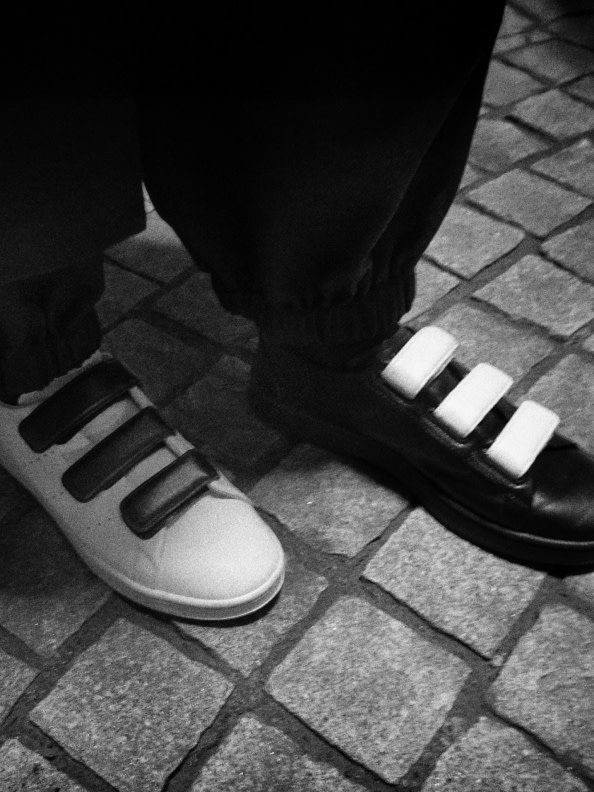 A pair of black dress shoes and a pair of white sneakers on a tiled floor, creating a striking contrast in the monochrome setting.