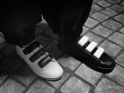 The image shows a pair of black-and-white shoes on a tiled floor, with the background appearing to be a dark and shadowy environment.