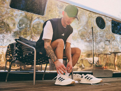 A person in a black tank top and shorts is sitting on a chair in front of a colorful, abstract mural background.