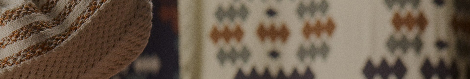 An abstract textural image showcasing a woven cream fabric with an orange striped pattern. In the background are other textured fabrics with geometric shapes on them.