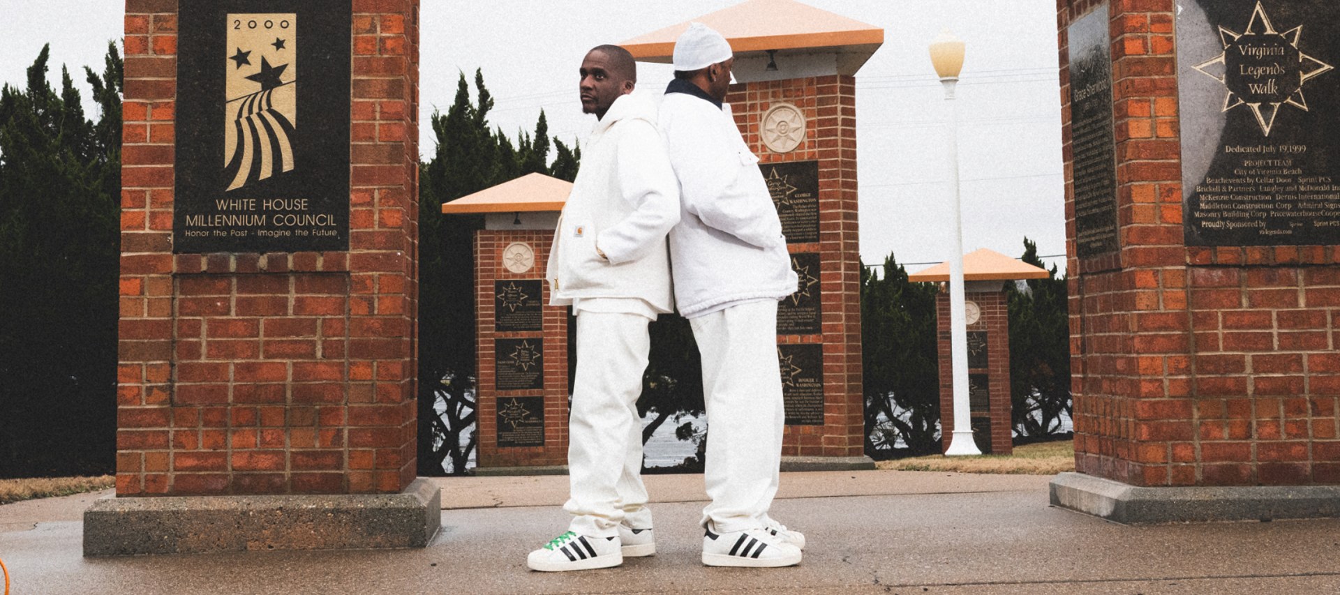 A person wearing a white outfit stands in front of a brick building with decorative elements, including a sign that says "White House Neighborhood Council".