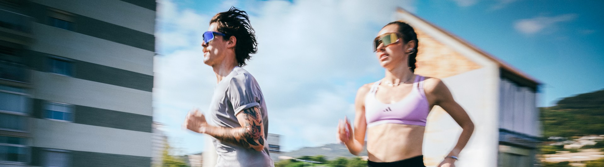 Deux personnes, un homme et une femme, se livrent à des activités physiques à l'extérieur, avec un paysage urbain visible en arrière-plan.