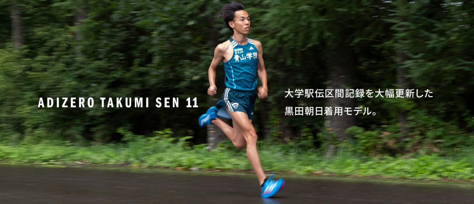 A young man in a blue athletic jersey and shorts is running on a path surrounded by lush green foliage.
