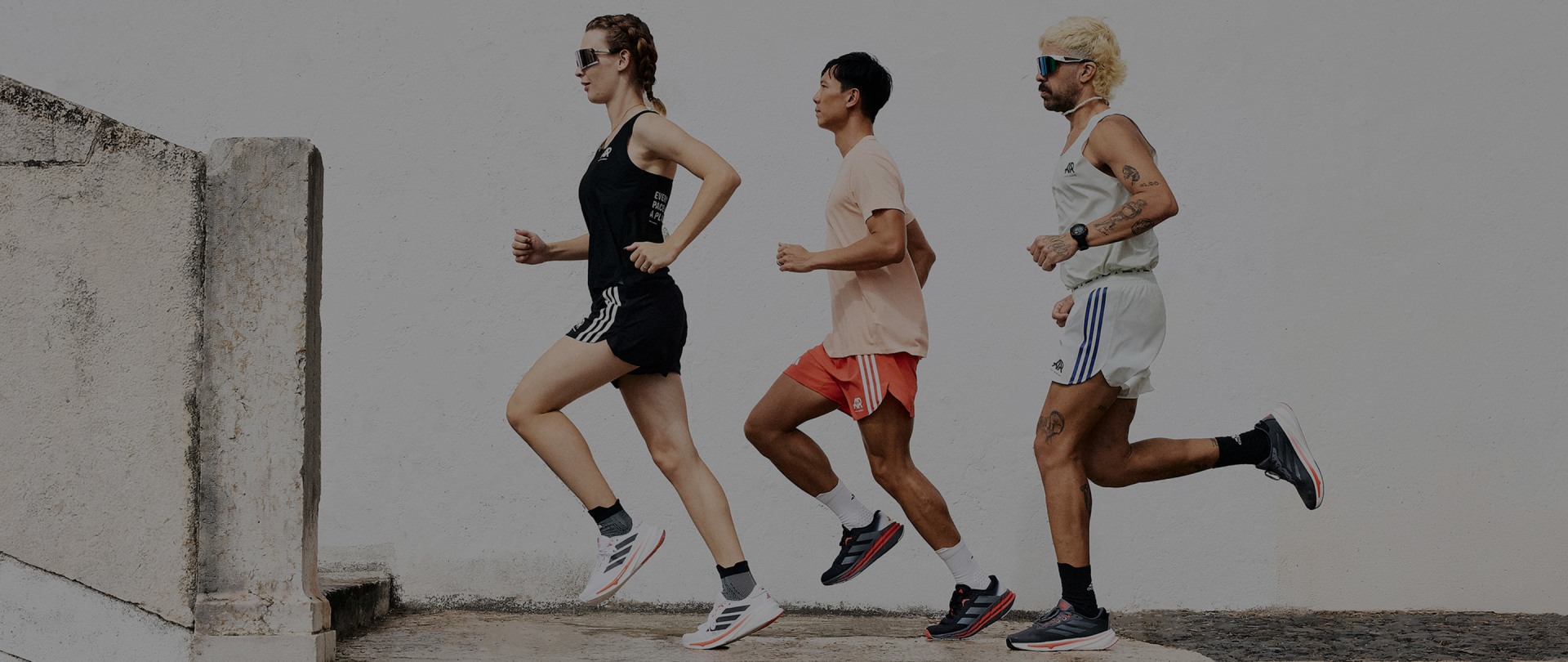 Three individuals, dressed in athletic attire, are running together against a plain background.