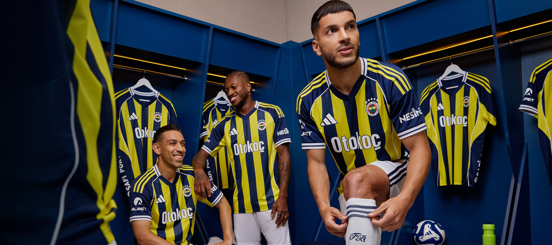 The image shows a group of soccer players in a locker room, wearing the yellow and blue uniforms of the Fenerbahçe football club.
