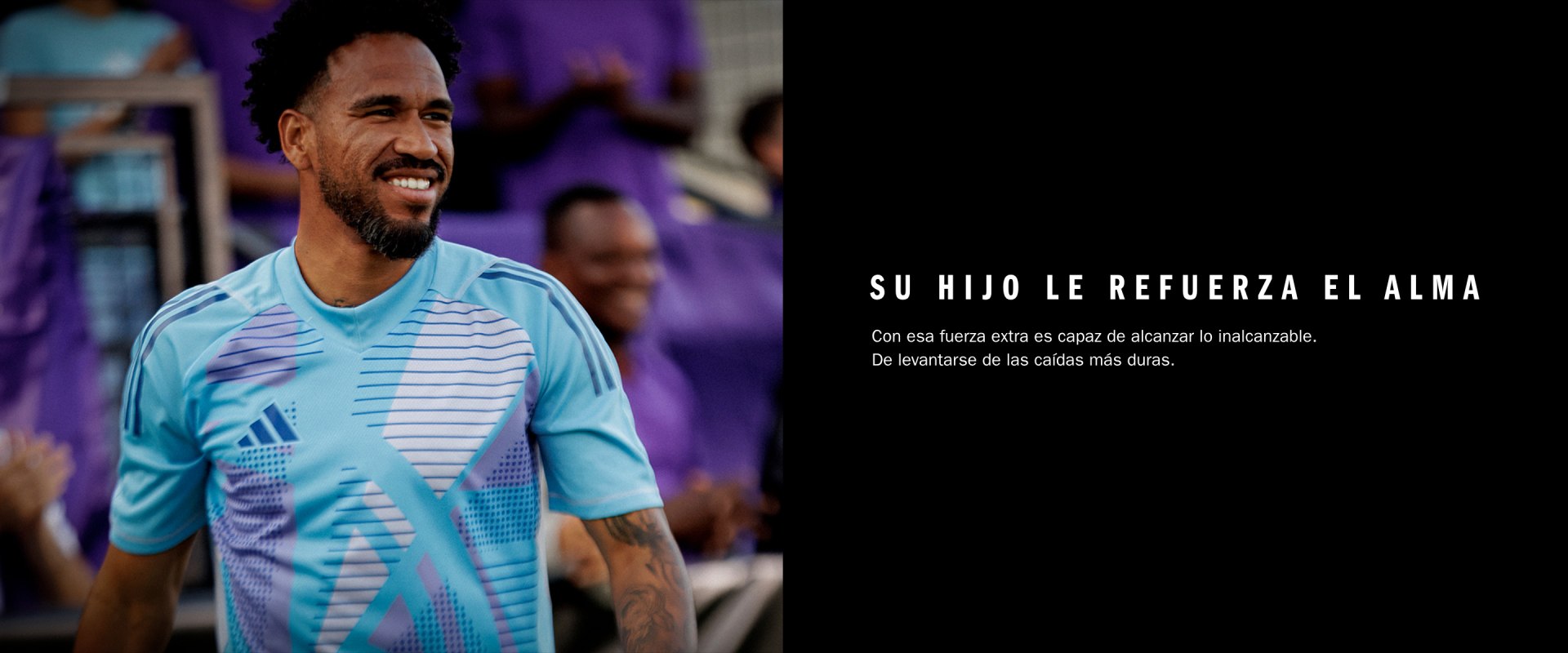 The image shows a smiling man wearing a light blue and white striped shirt, standing in front of a colorful, graffiti-covered wall.