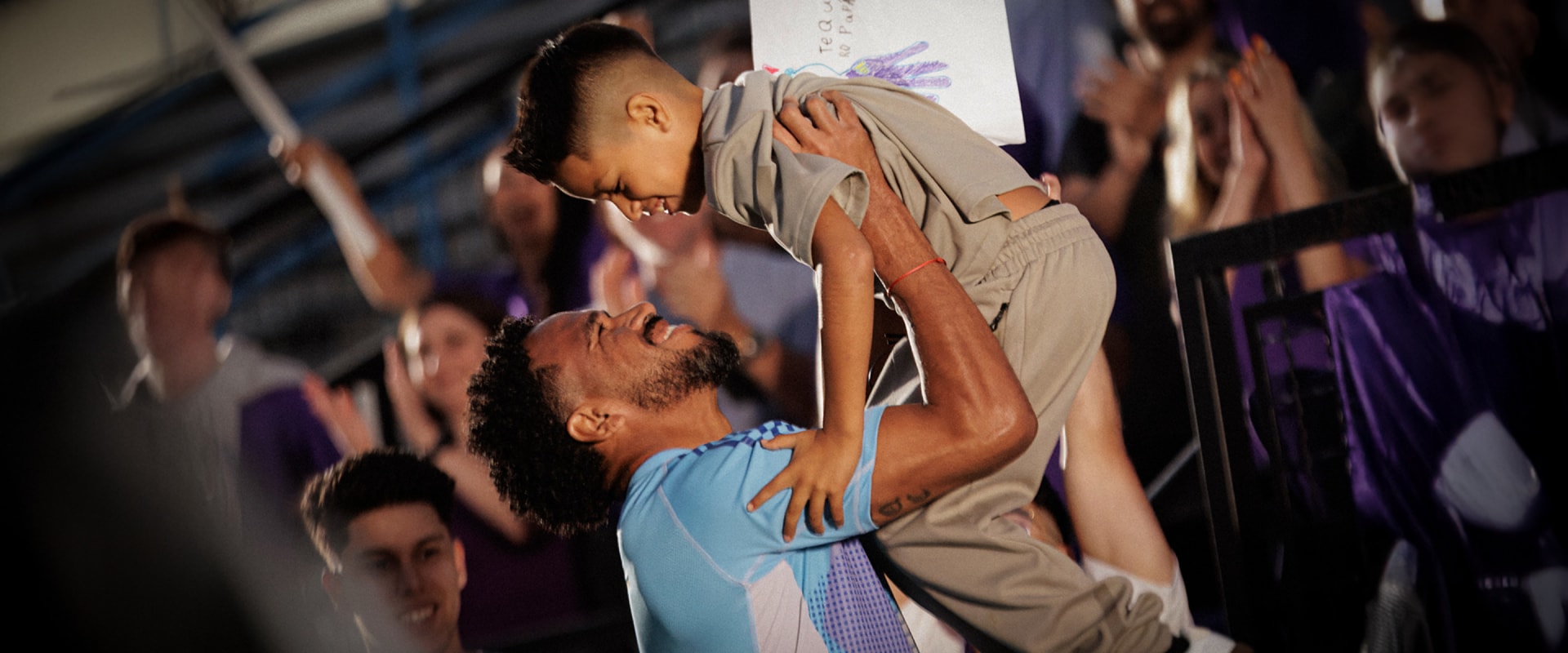 Two individuals are embracing on a stage, surrounded by a crowd of people in the background.