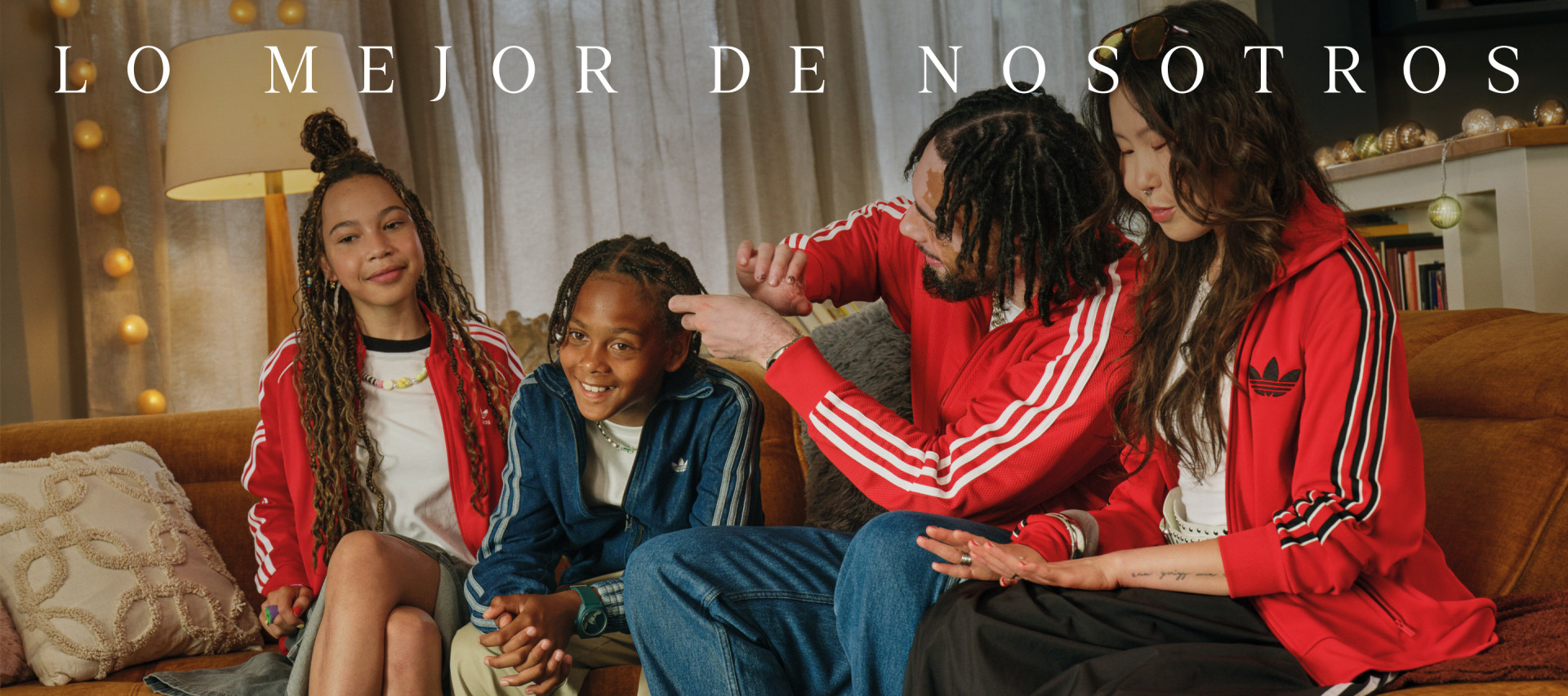 The image shows a group of young people, likely friends, sitting together on a couch. They are all wearing red jackets or hoodies, and the background appears to be a cozy indoor setting with curtains and lighting.