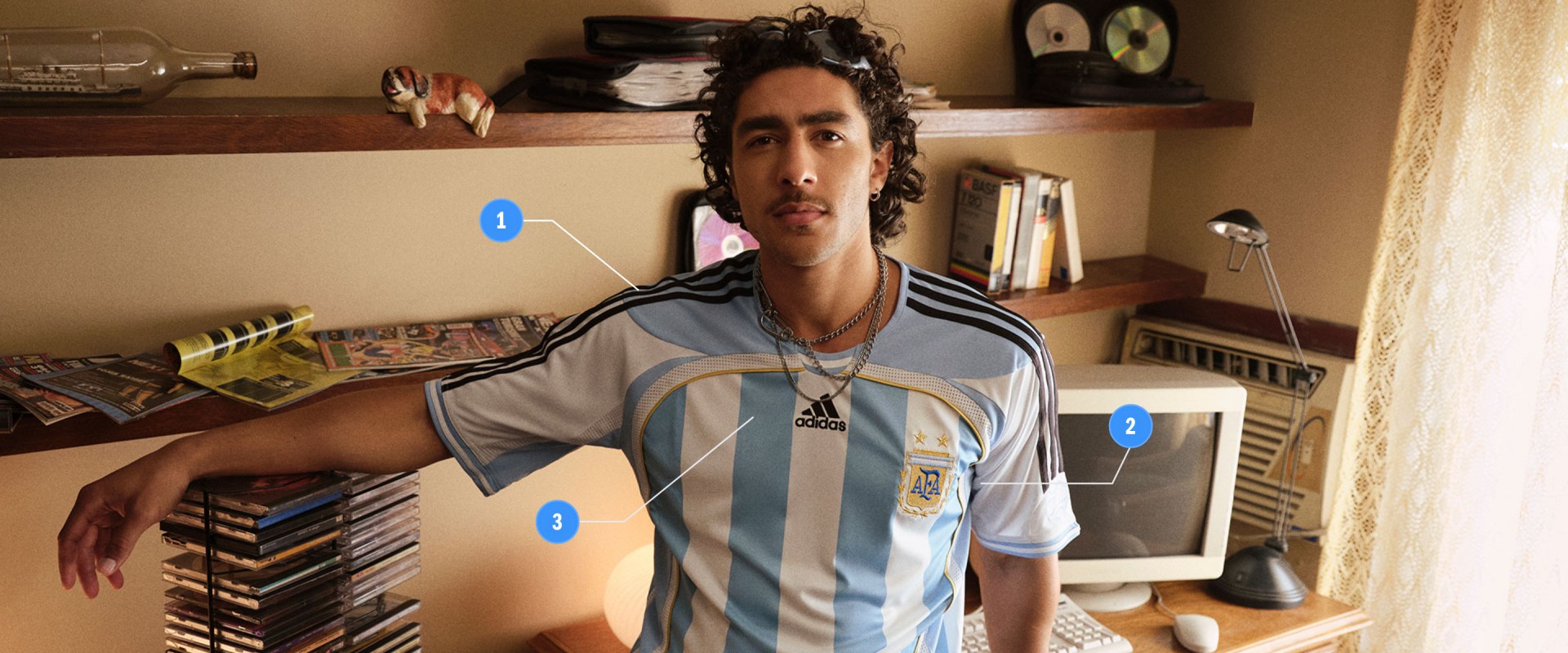 A young man wearing an Adidas jersey is standing in a room filled with shelves, books, and various other items.