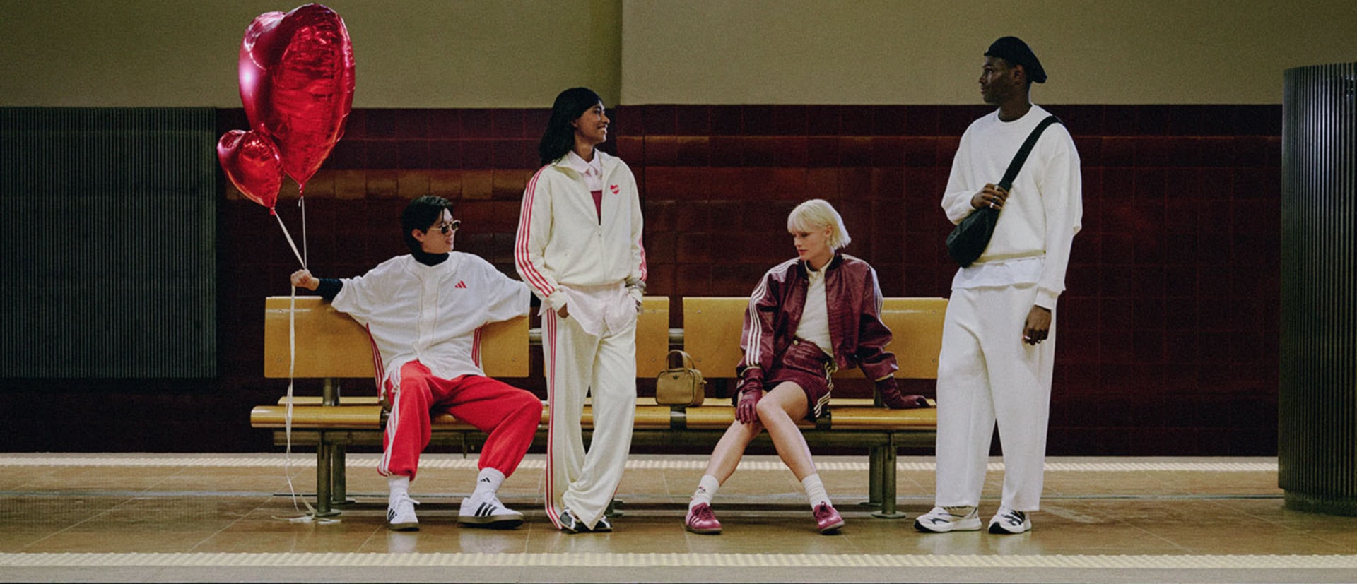 A group of individuals dressed in stylish, colorful outfits stand on a stage, with a large red heart-shaped balloon in the foreground.