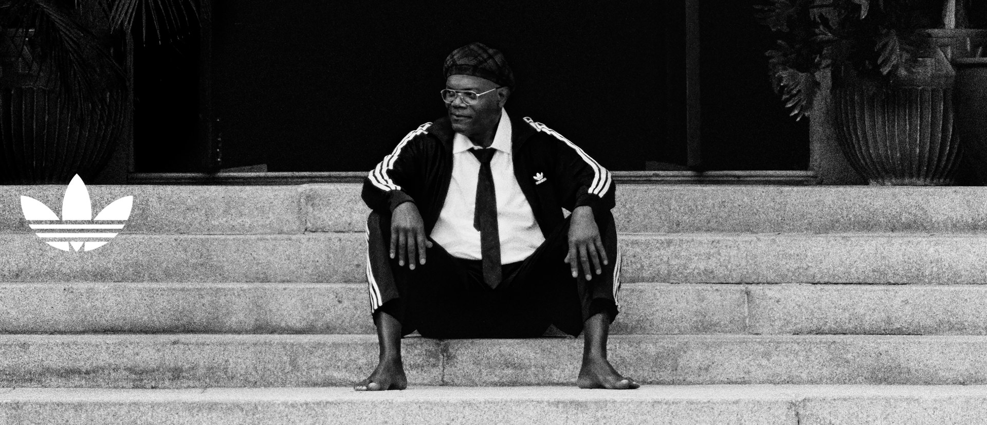 A person wearing a suit and tie sits on a set of stairs, with a dark background behind them.