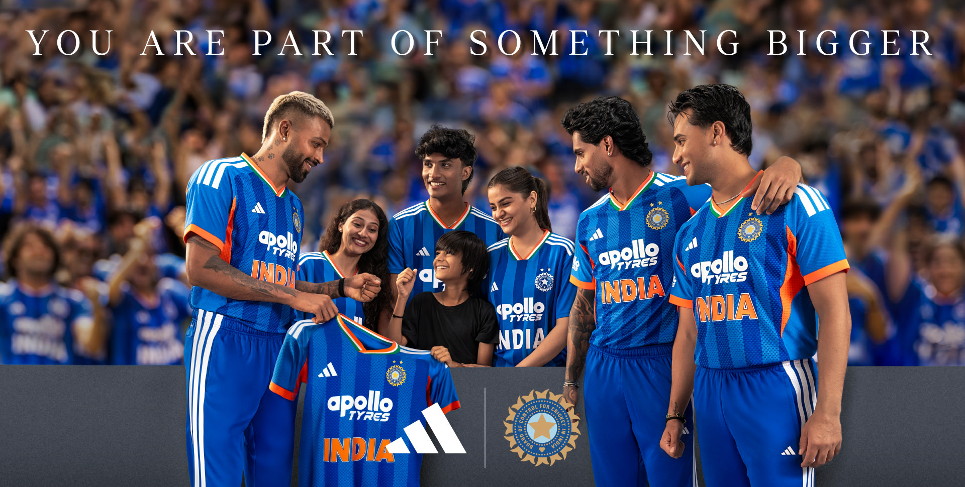 A group of people wearing blue cricket jerseys with the Indian national cricket team logo, standing together in a stadium setting with a large crowd in the background.