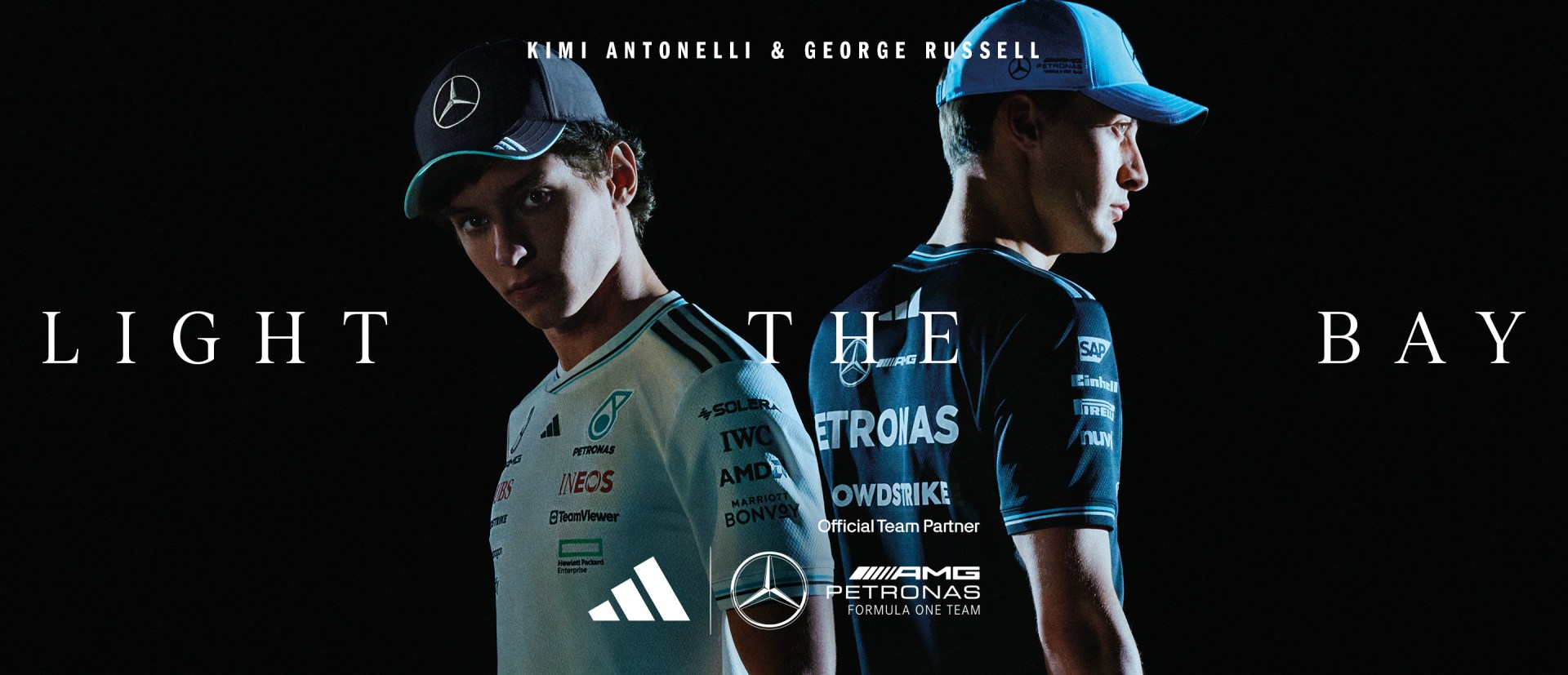 Two individuals wearing Mercedes-AMG Petronas Formula One team uniforms and caps stand against a dark background.
