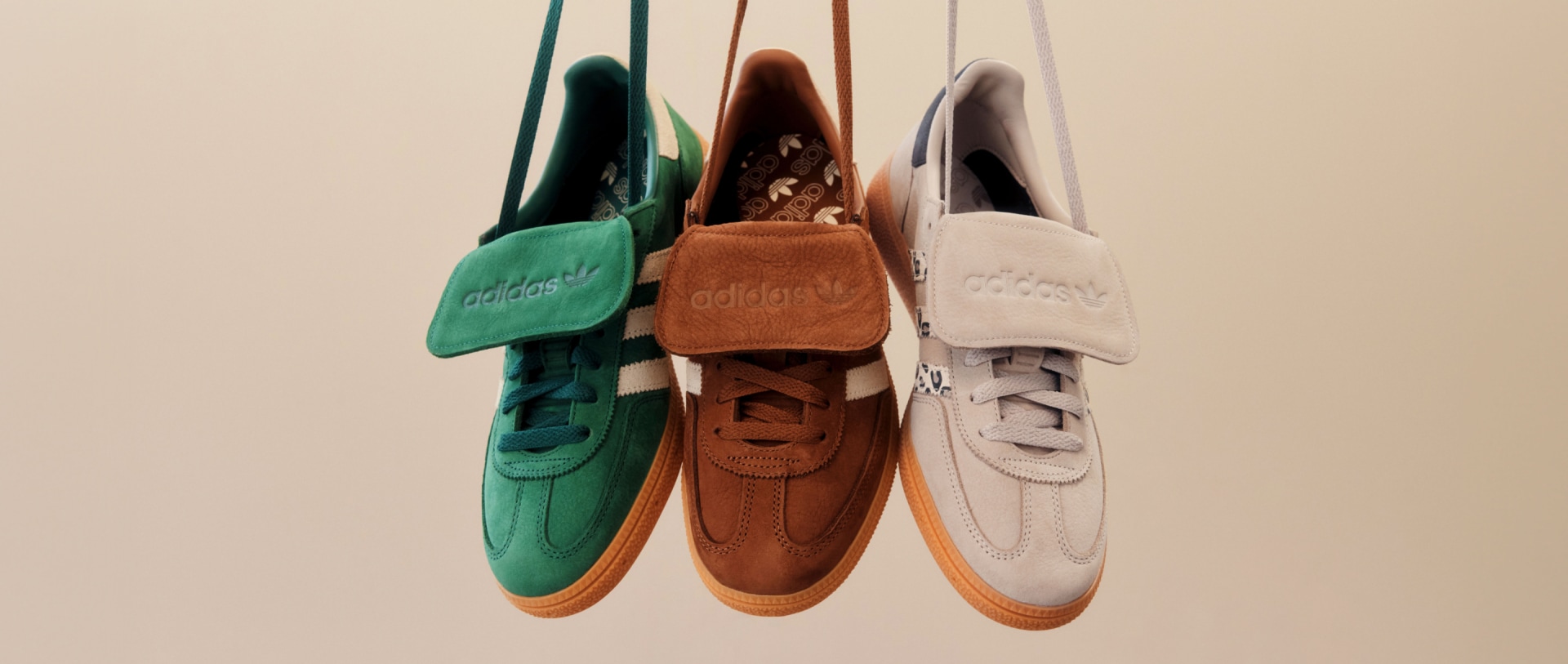 Een collectie met verschillende gekleurde en gestyleerde adidas sneakers, waaronder groene, bruine en grijze, die aan een muur hangen.