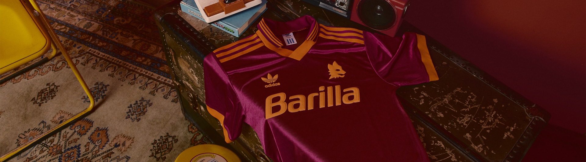 A vibrant red and orange Barilla soccer jersey is displayed on a shelf, surrounded by various other items in the background.