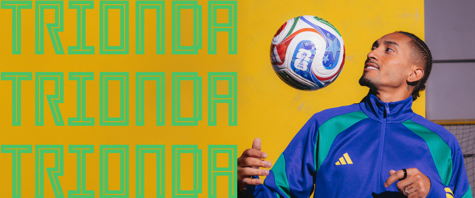 A young man in a blue and green athletic jacket stands in front of a vibrant yellow and green background, holding a rugby ball and looking up at it with a focused expression.