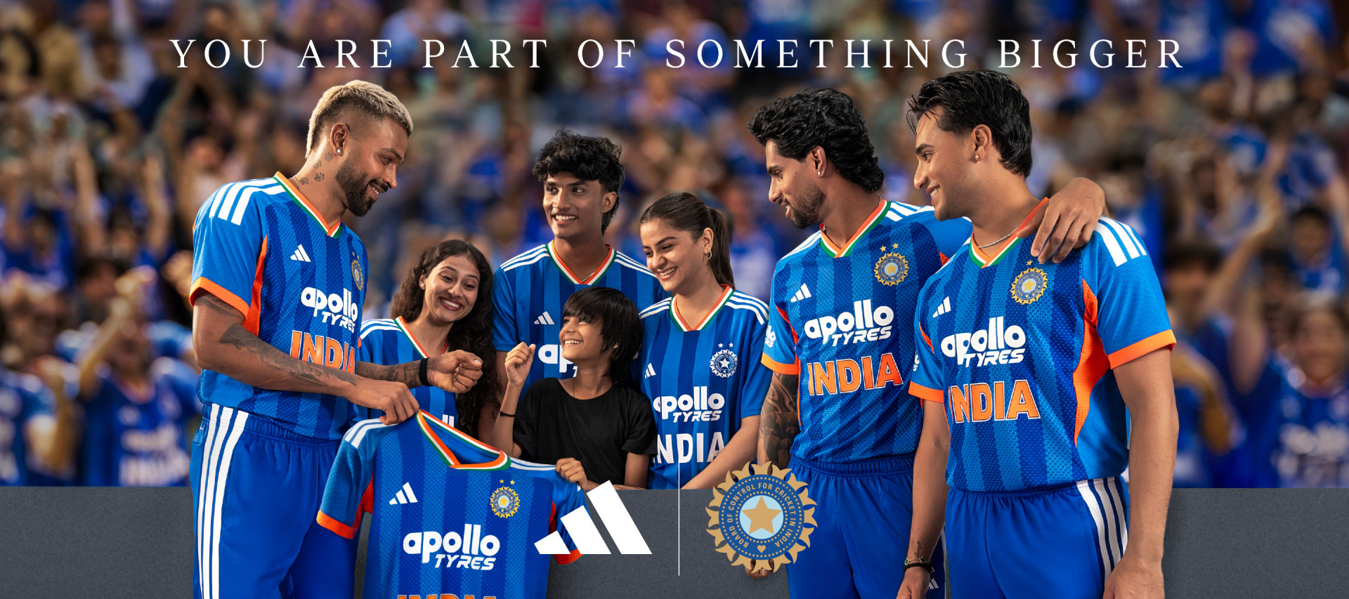 A group of people wearing blue cricket uniforms with the "Apollo Tyres" logo, standing together and embracing, with a large crowd visible in the background.