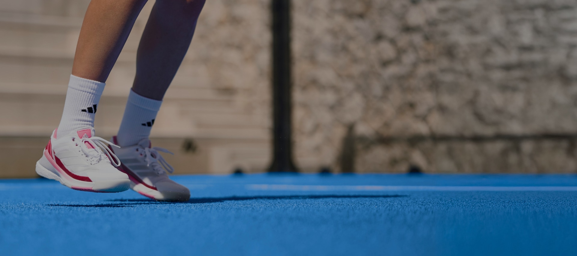 The image shows a person's legs and feet wearing athletic shoes standing on a blue exercise mat against a blurred background.
