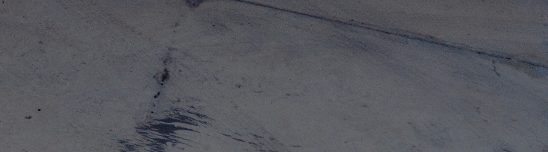 A dark, textured surface with faint, wispy patterns and a sense of depth and movement.