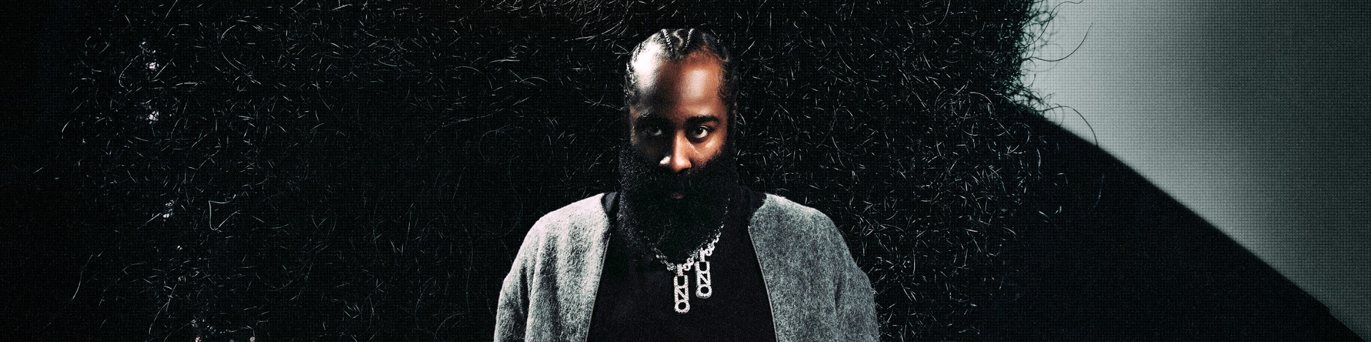 A person with a long beard and intense gaze emerges from a dark, textured background.