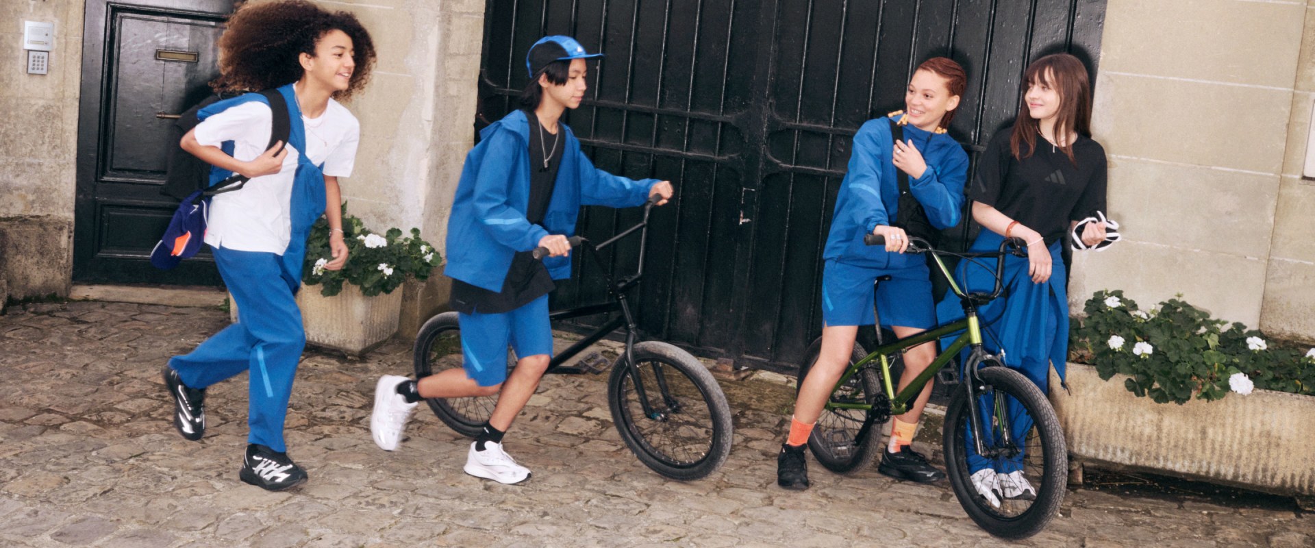 A group of young people, dressed in matching blue outfits, stand together in front of a wooden structure, with one person riding a bicycle.