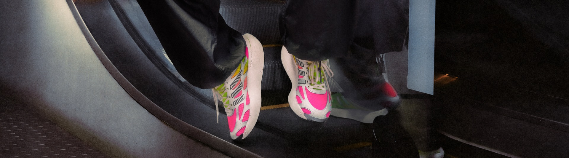 Vibrant pink and yellow sneakers stand out against a dark, shadowy background, creating a striking visual contrast.