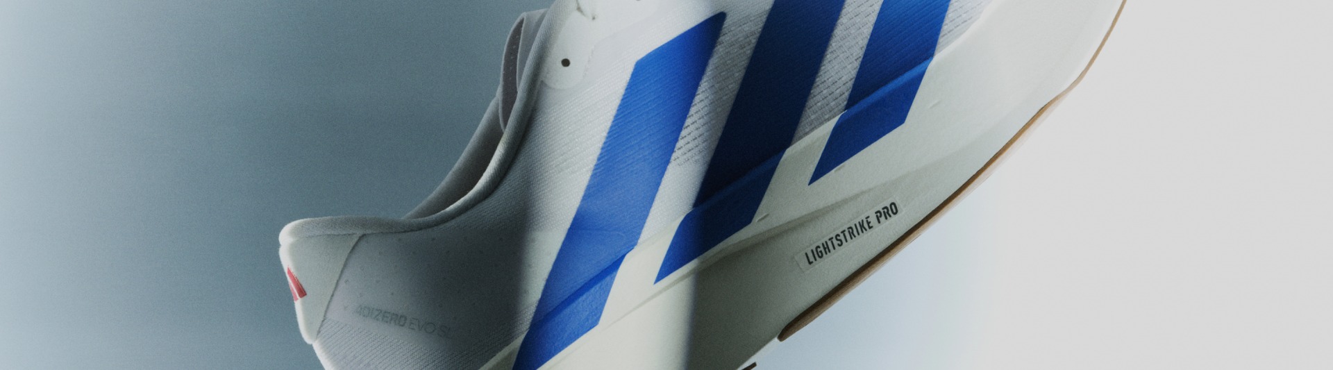 Close-up image of white Adizero EVO SL with blue stripes, showcasing the Lightstrike Pro outsole.