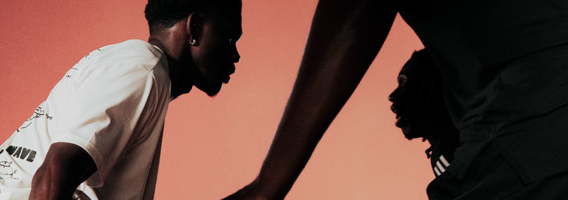 アンソニー・エドワーズがホワイトのアディダスのシャツに身を包み、ブラックのアディダス ショーツに身を包んでドリブルをする様子が描かれたバスケットボールの試合中のクローズアップ。暖かい色の背景に、ブラックのアディダスのウェアを着た選手たちが守備にあたっている様子。