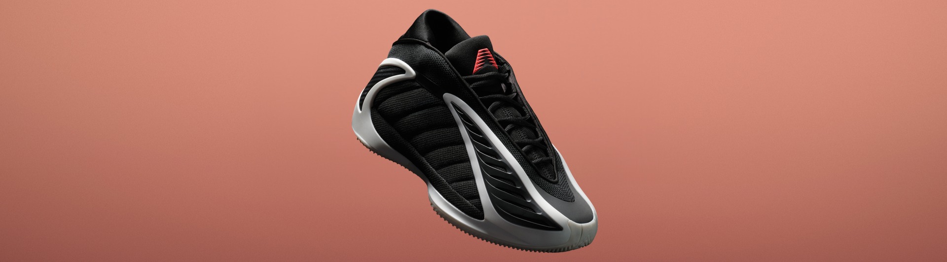 ピーチカラーの背景に赤いアクセントが映える、ブラックとシルバーのアスレチックシューズ。