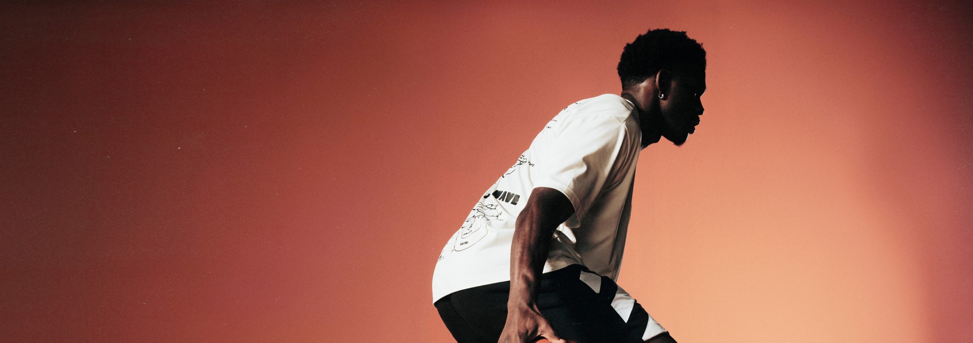 A person wearing a white shirt stands against a warm, orange-toned background.