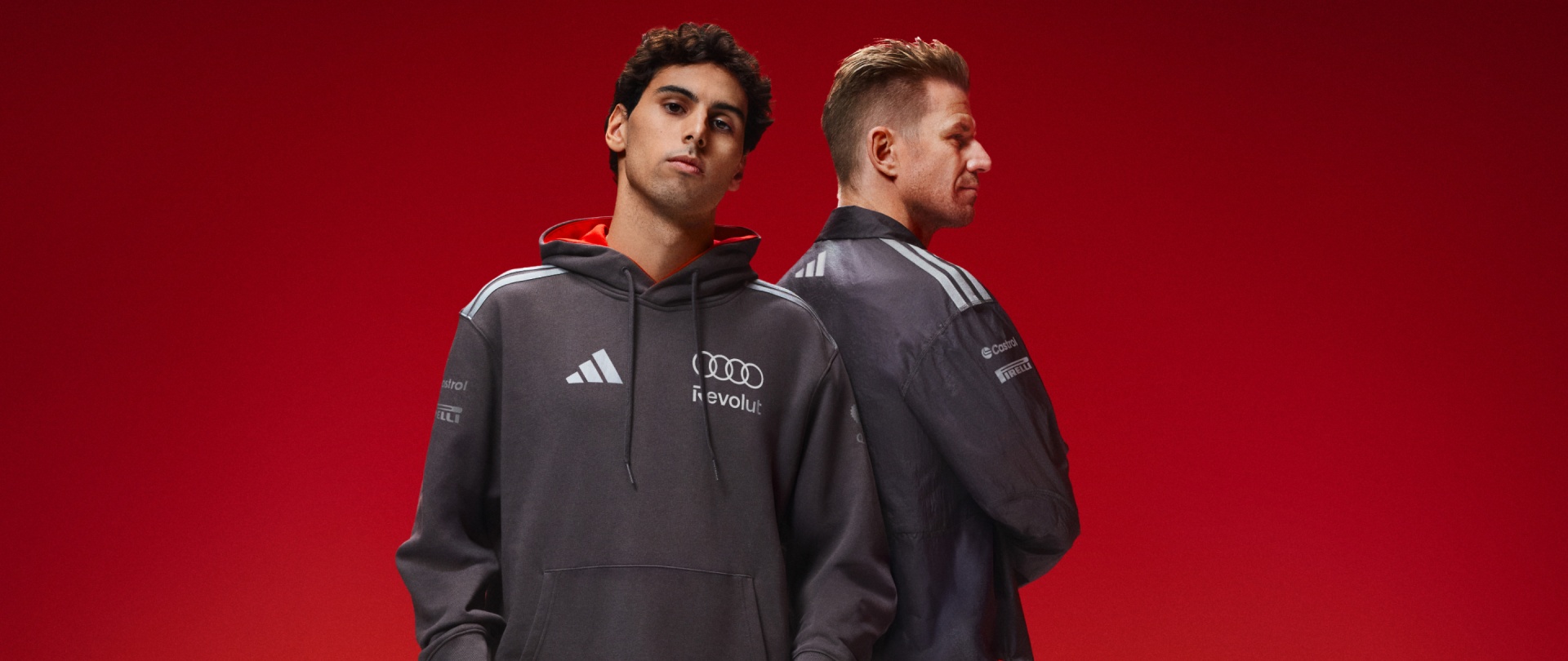 To unge mænd iført grå hættetrøjer med Audi-logoet står på en strålende rød baggrund.