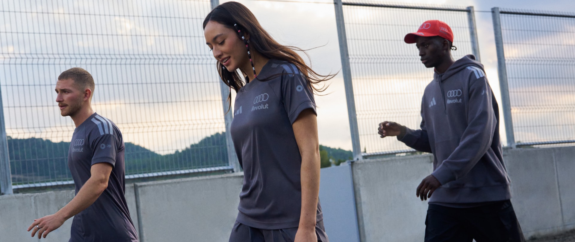 Billedet viser en gruppe mennesker, herunder en kvinde med langt hår og to mænd, der står foran et indhegnet område.