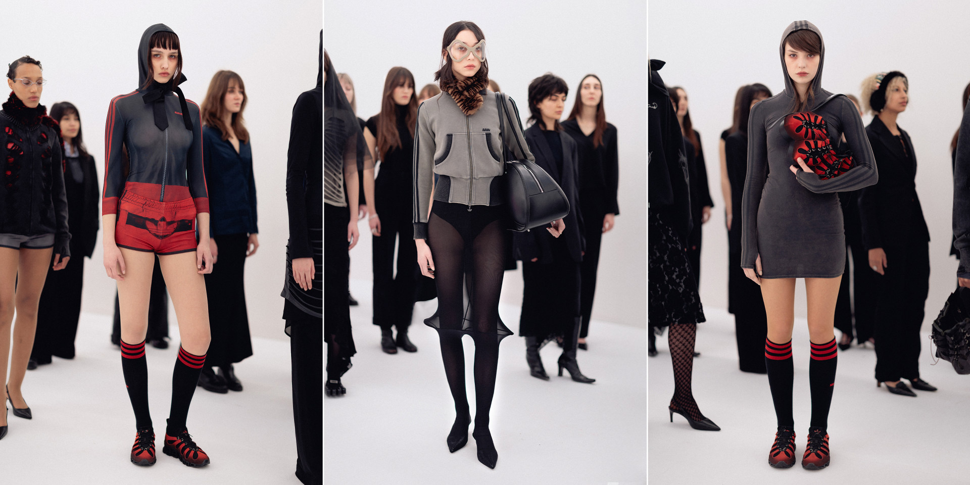 A group of fashionably dressed models, wearing dark, avant-garde clothing, stand against a plain white background, creating a striking and dramatic visual display.